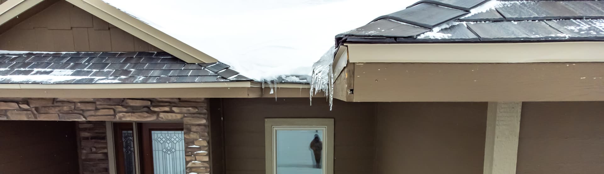 Thick ice dam and icicles forming along the eaves of a suburban Chicago home in winter — representing the roof damage ice dams cause